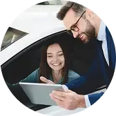 Сотрудник демонстрирует данные на планшете женщине, сидящей за рулём автомобиля.