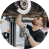 Механик в рабочей форме ремонтирует автомобиль, стоя под поднятым авто и используя инструмент для закручивания гаек.