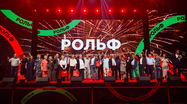 Мероприятие с участием людей на сцене и надписью 'РОЛЬФ' на заднем плане.