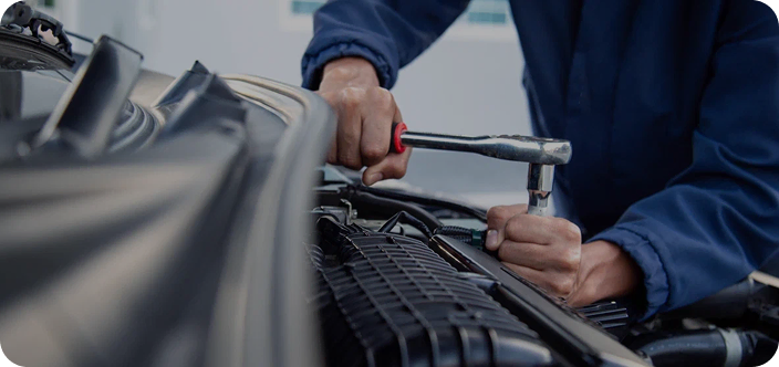 Механик в синей рабочей одежде ремонтирует двигатель автомобиля ключом.