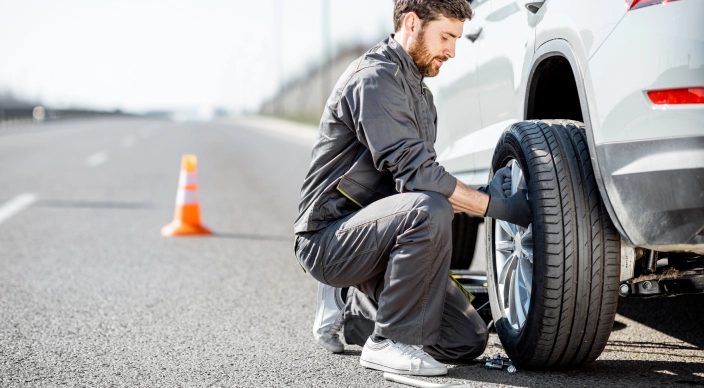 Мужчина чинит колесо автомобиля на дороге.