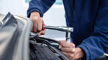 Работник автосервиса выполняет техническое обслуживание двигателя с помощью инструмента.