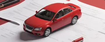 Красная игрушечная машинка стоит на документах, связанных с автомобилем