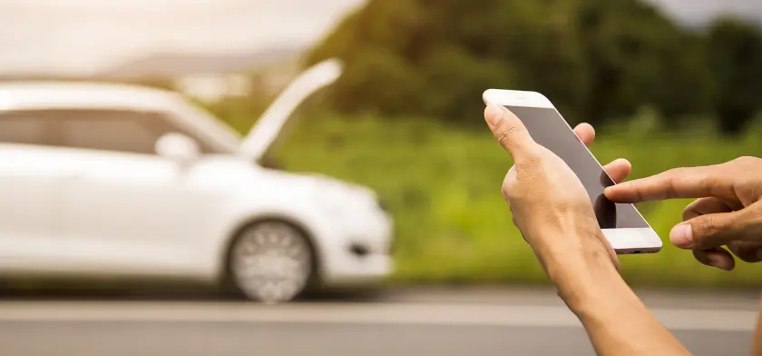 Человек держит смартфон с размытым белым автомобилем на заднем плане