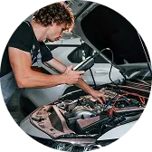 Мужчина в рабочей одежде проводит ремонтные работы под капотом машины.