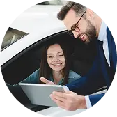 Сотрудник демонстрирует данные на планшете женщине, сидящей за рулём автомобиля.