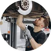 Механик в рабочей форме ремонтирует автомобиль, стоя под поднятым авто и используя инструмент для закручивания гаек.