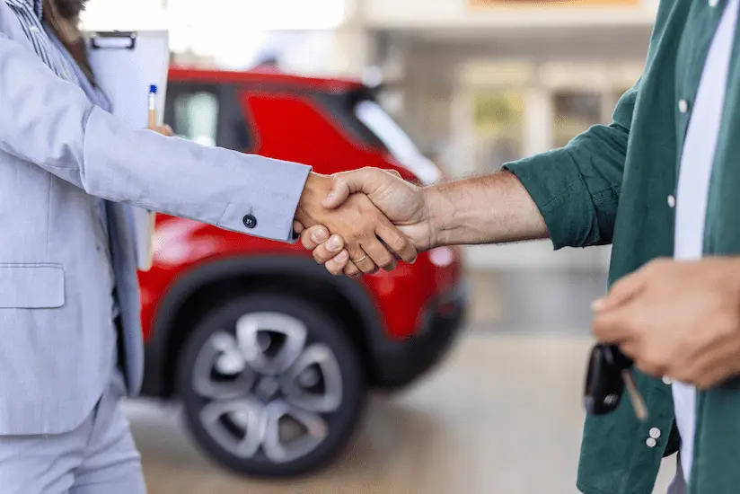 Рукопожатие двух человек в автосалоне на фоне красного автомобиля.