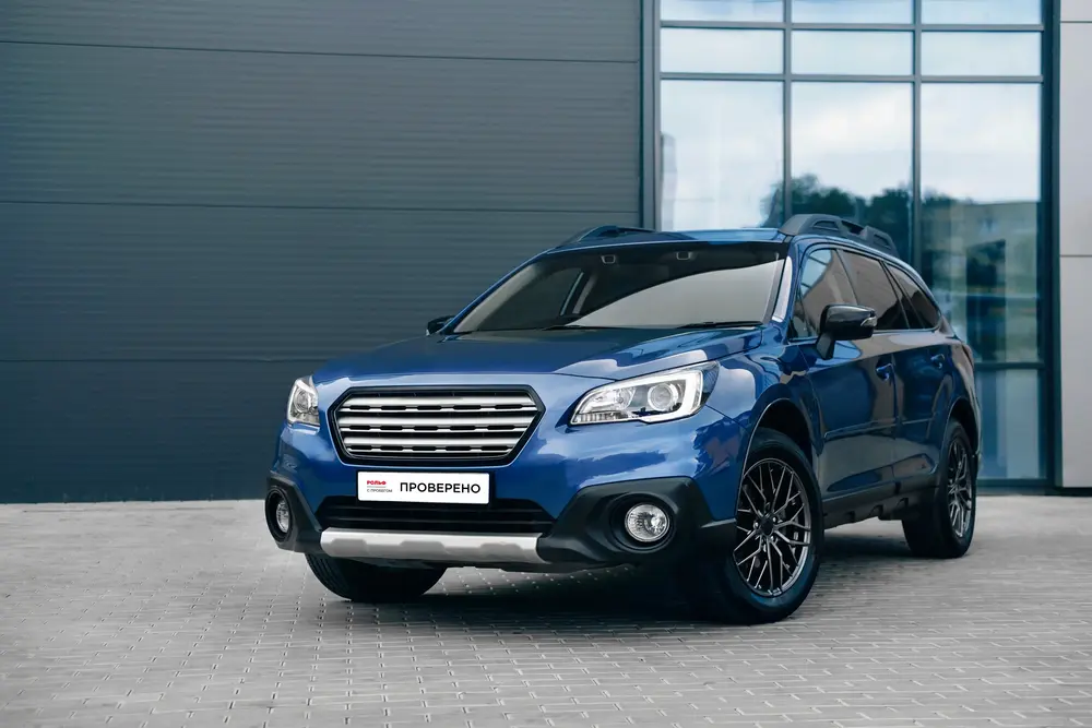 Cиний внедорожник стоит перед зданием с панорамными окнами.