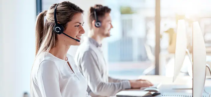 Два человека, которые работают в call-центре, используя компьютеры и гарнитуры для общения с клиентами.